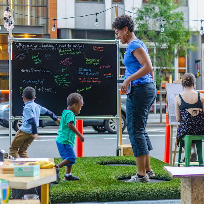 A mother and her kids jump on trampolines at PARK(ing) Day