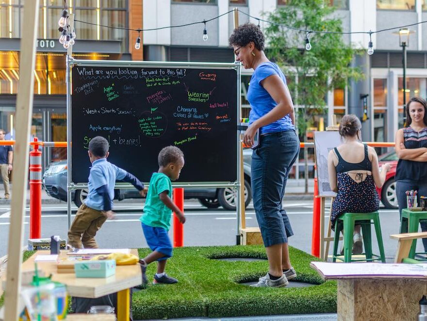 A mother and her kids jump on trampolines at PARK(ing) Day