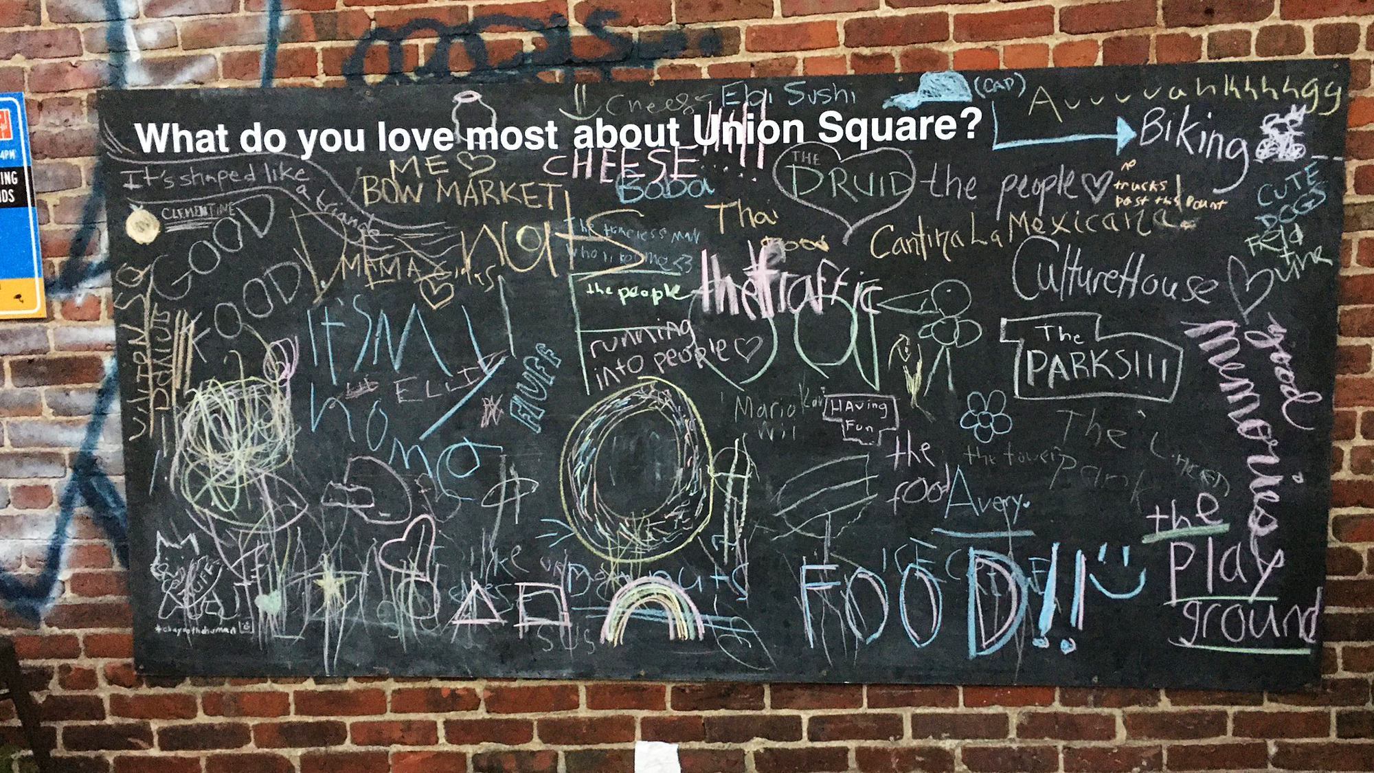 A chalkboard on a brick wall with the prompt "What do you love most about Union Square?" Various responses are written on the chalkboard with chalk.