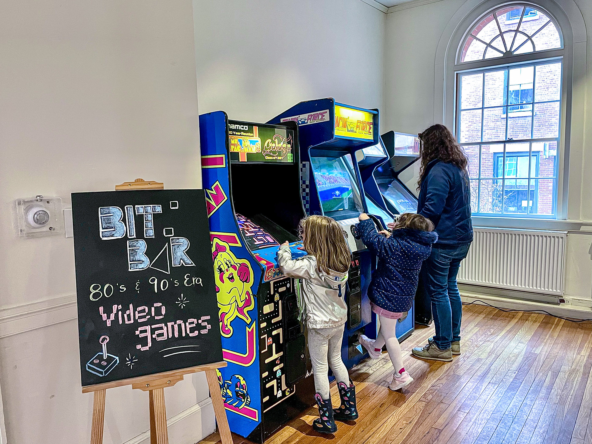 Two children and an adult stand and play vintage video games