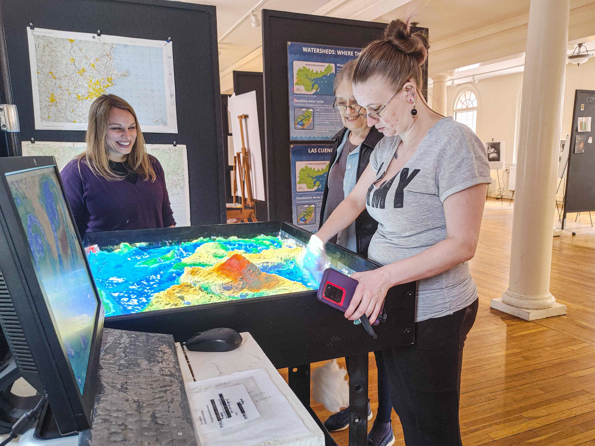 Three people stand around a sand table building up topographic forms.