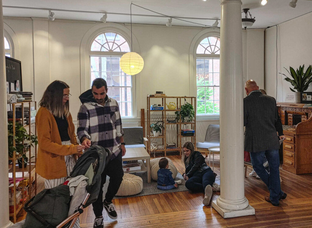 People standing around a cozy livingroom area while children play.