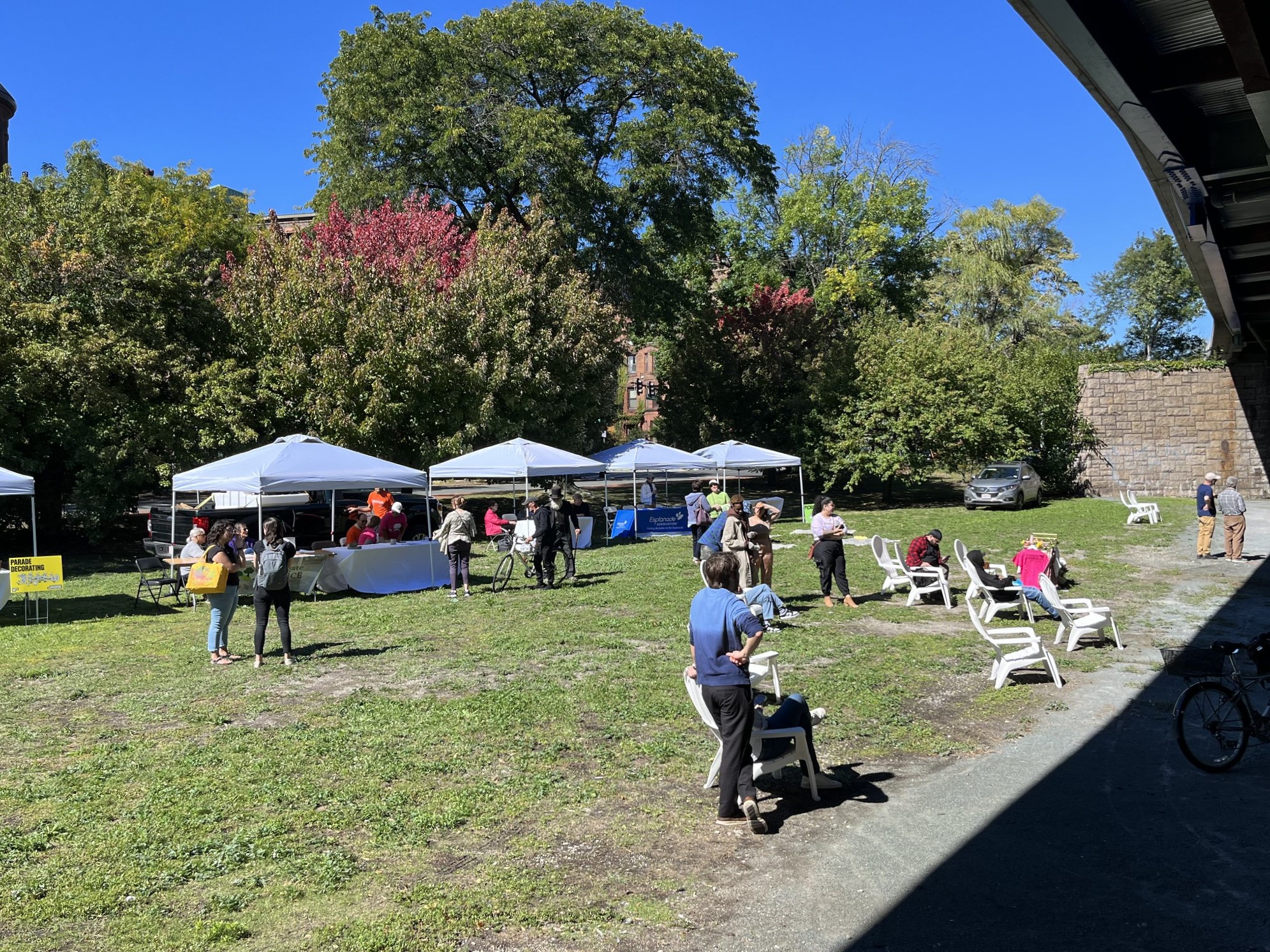 People sit and stand on a green area around tables and tents