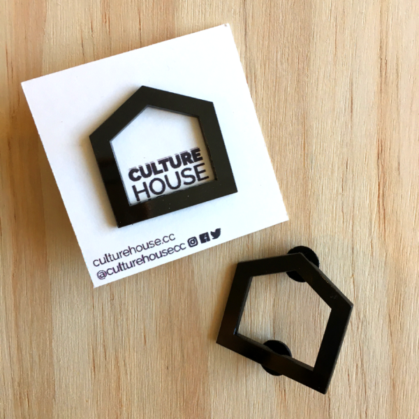 Two CultureHouse black enamel pins against a wooden background. The pins are in the shape of a black five point house.