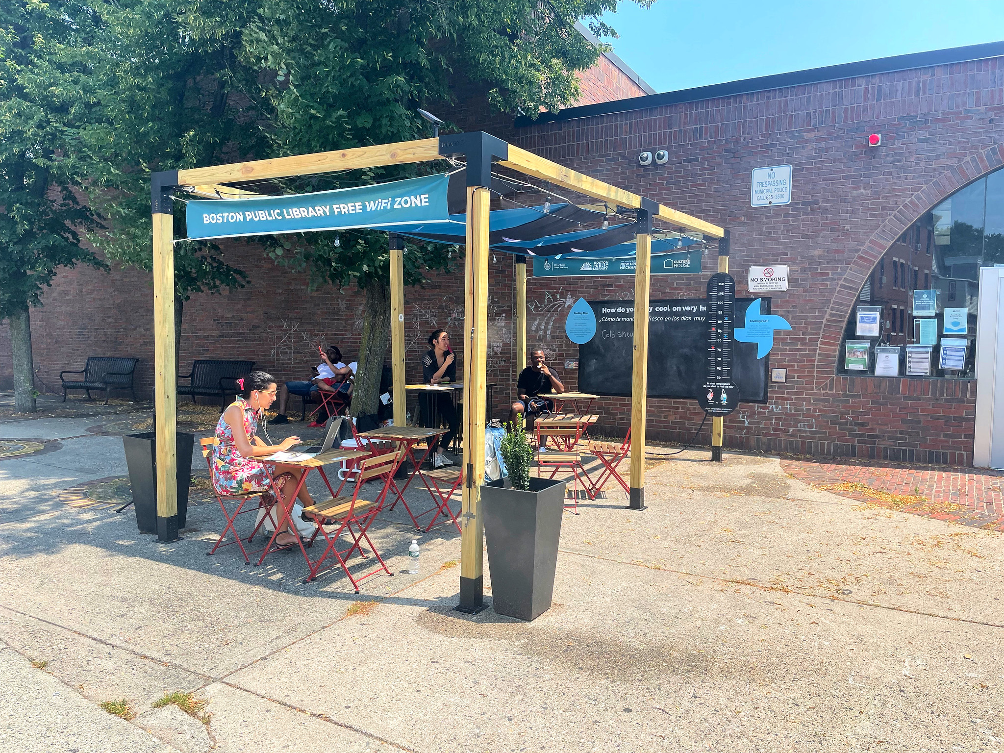 People sitting under built shade on chairs with tables by the Urban Heat installation