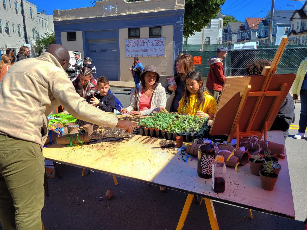 A man helps people pot small plants on a big table 