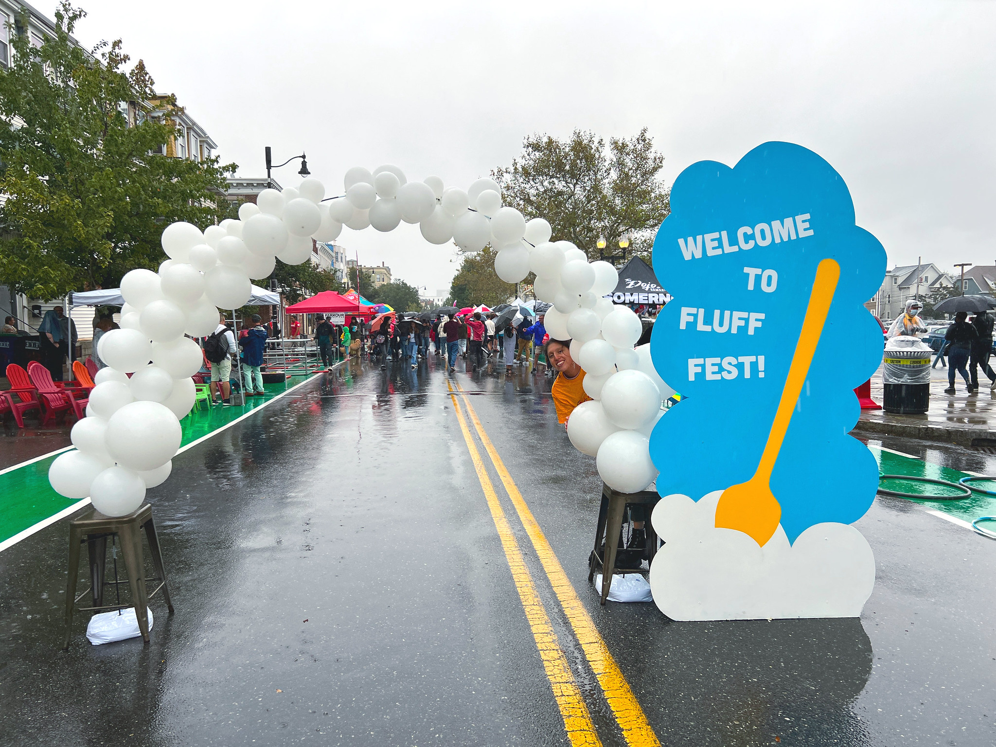 In the middle of a closed down street, a white balloon arch sits next to a tall sign that reads "Welcome to Fluff Fest!"