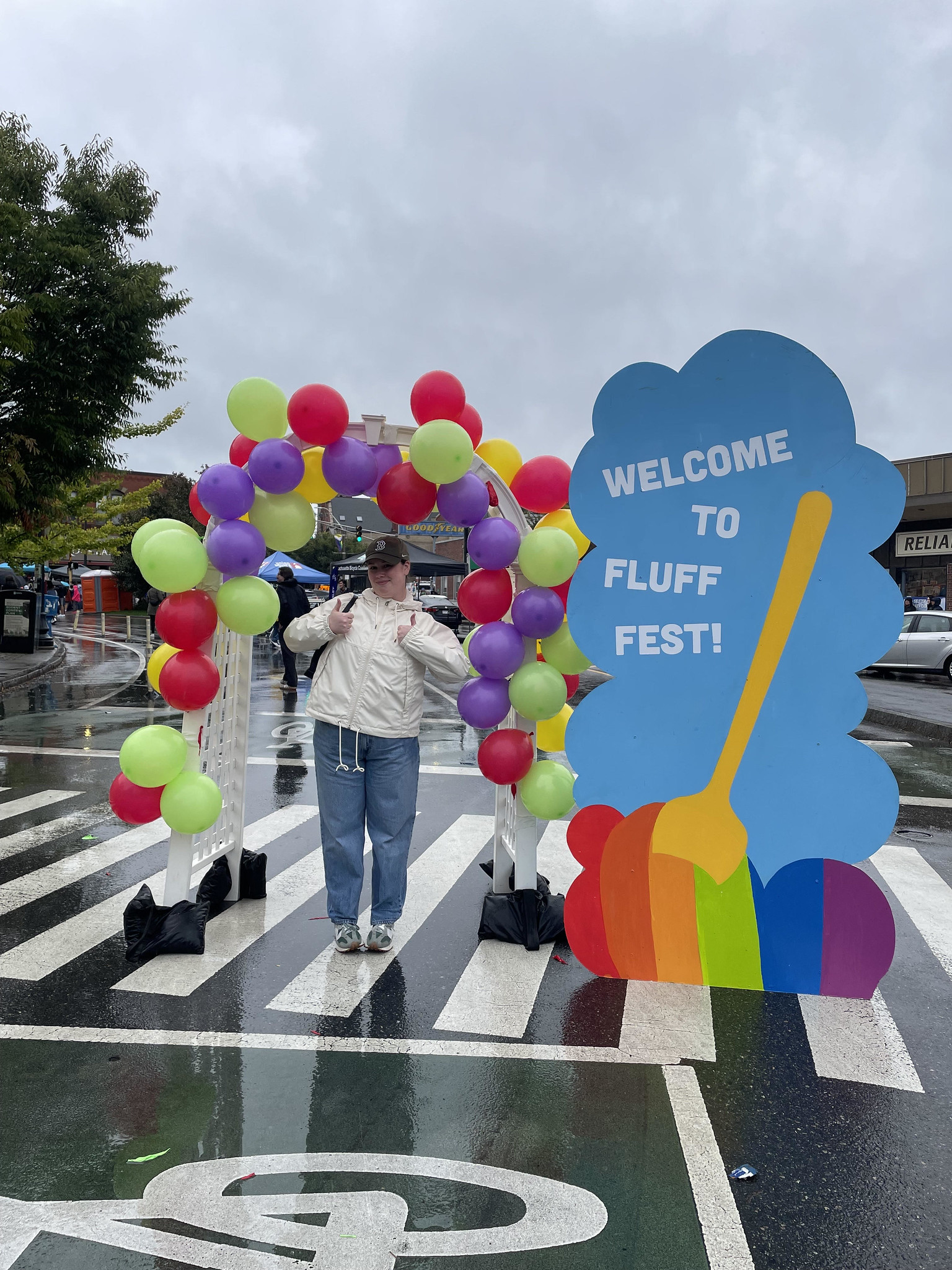 A person stands under a balloon covered archway next to a sign that reads "Welcome to Fluff Fest"