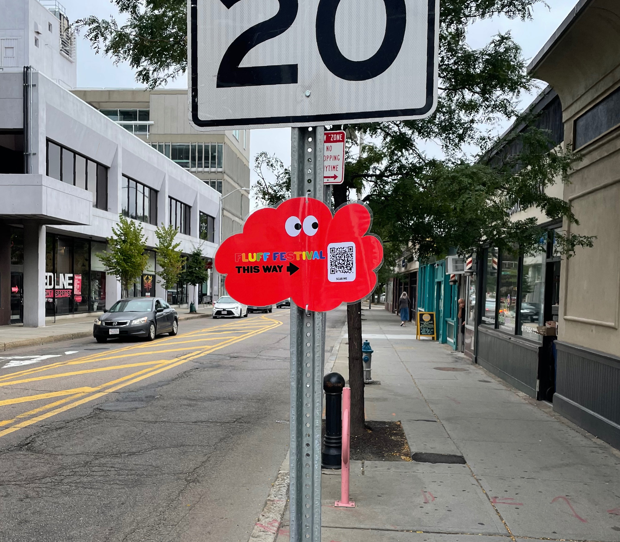 A red cloud sign attached to a sign post reads "Fluff Festival This way" next to a QR code