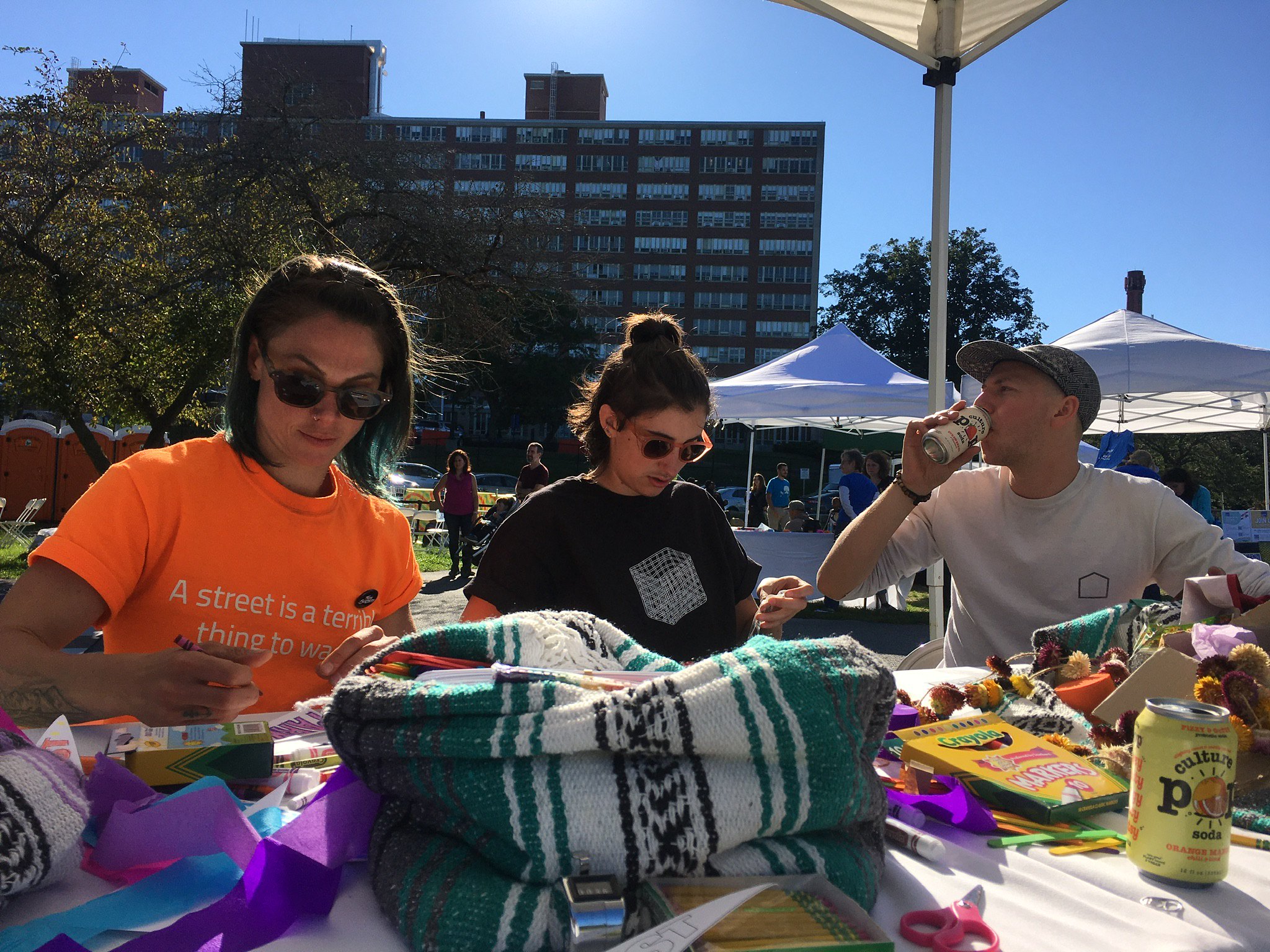 Three people sit at a craft table, drawing and drinking seltzer