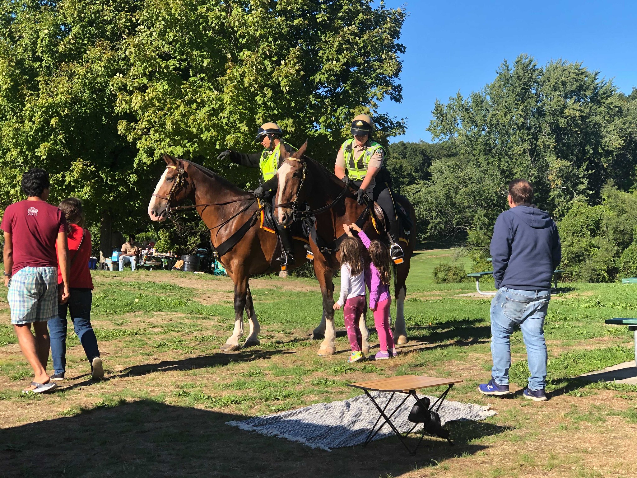 Two children approach rangers on horses to pet the horse while a parent looks on.