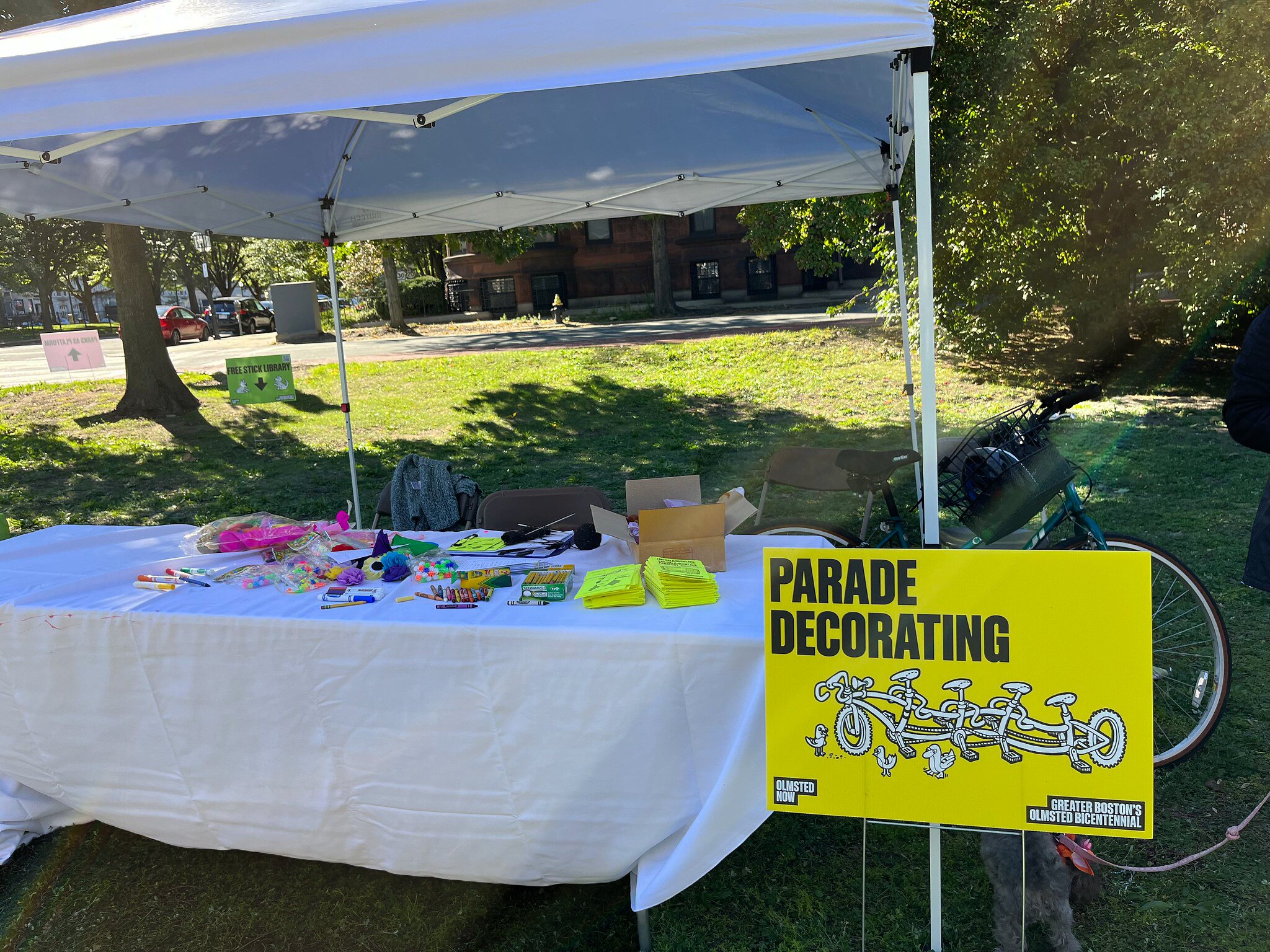 A table covered in craft materials and scavenger hunt pamphlets. A bike is next to a sign that says "Parade Decorating"