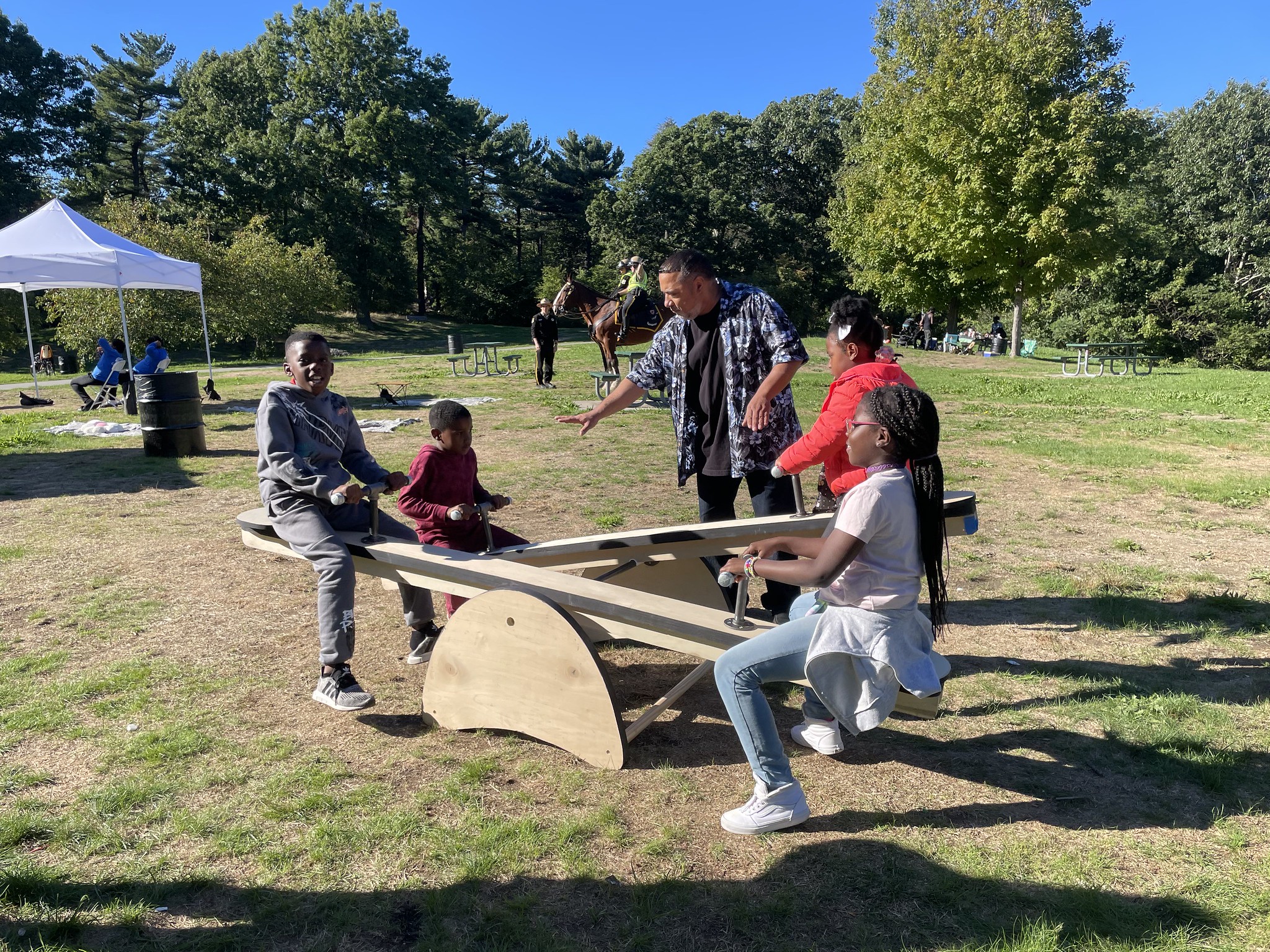 Kids playing on a see saw while an adult watches