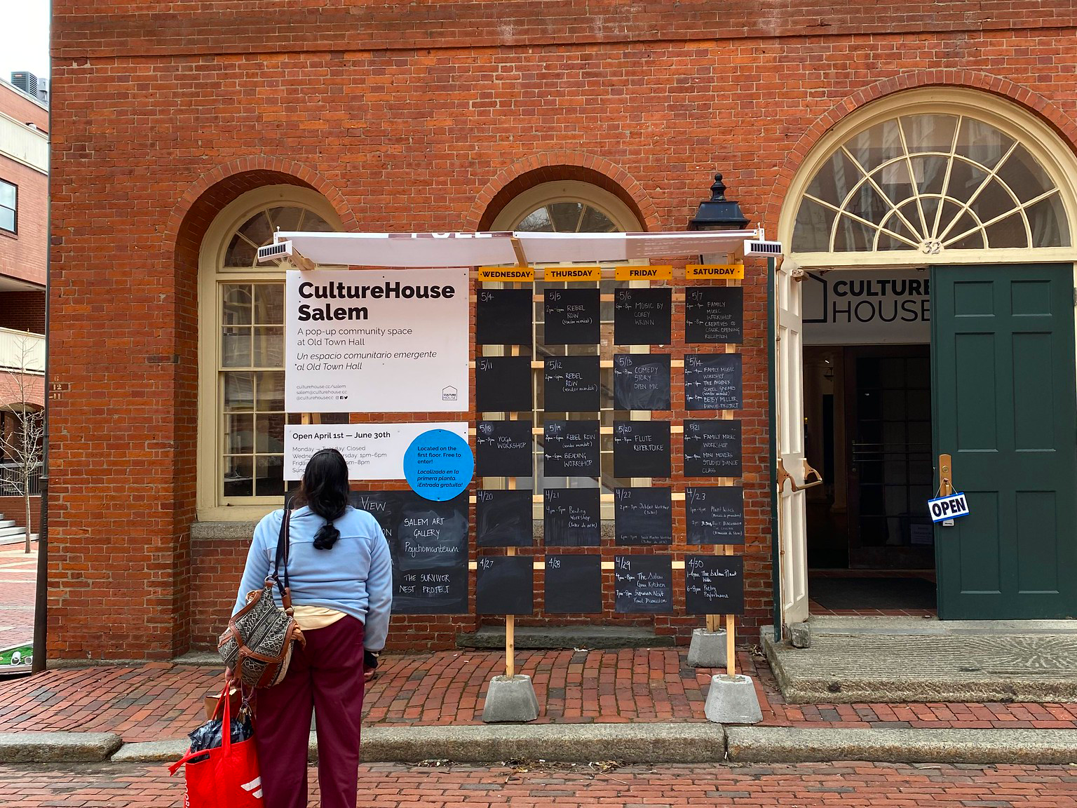 A woman with a totebag stands in front of an event calendar listing activities at CultureHouse Salem outside of the Old Town Hall.