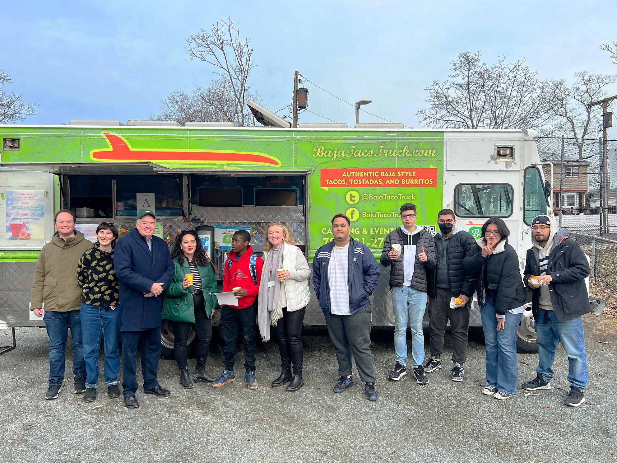 Members of MONUM, CultureHouse, community members, and State Representative stand in front of Baja Taco Truck holding hot cocoa and churros.