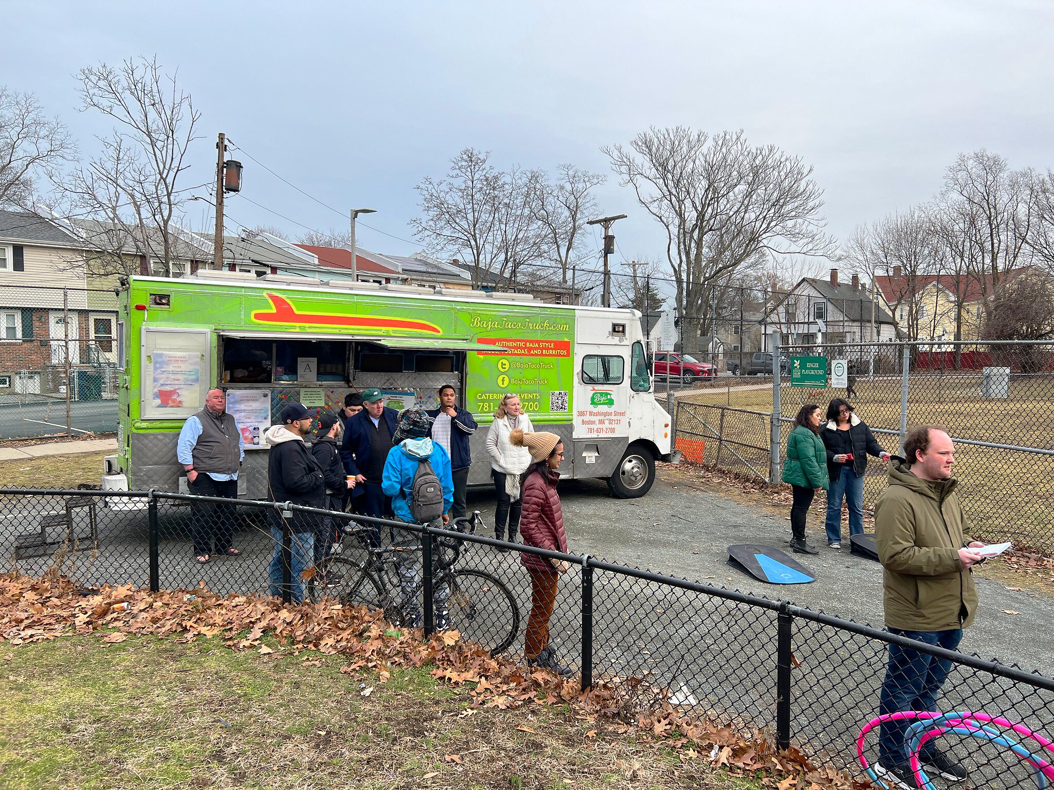 A group of people stand in front of a food truck mingling and playing cornhole