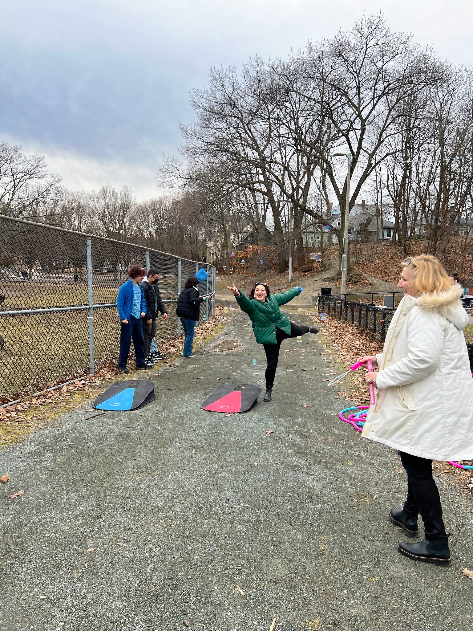 A woman gleefully throws a cornhole bag while a woman and a few teenagers look on