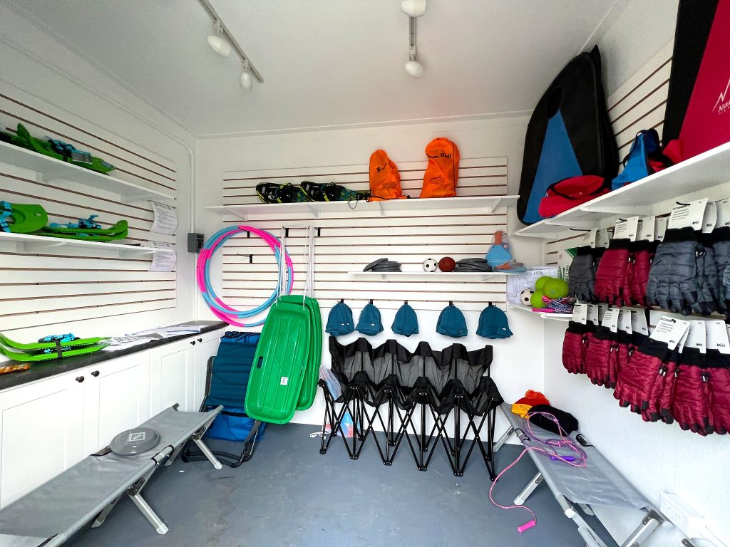 Images of a well organized shed stocked with games and seating. Gloves and hats line the walls while sleds, hula hoops, and snow shoes hang on the walls. Foldable seating lines the ground.