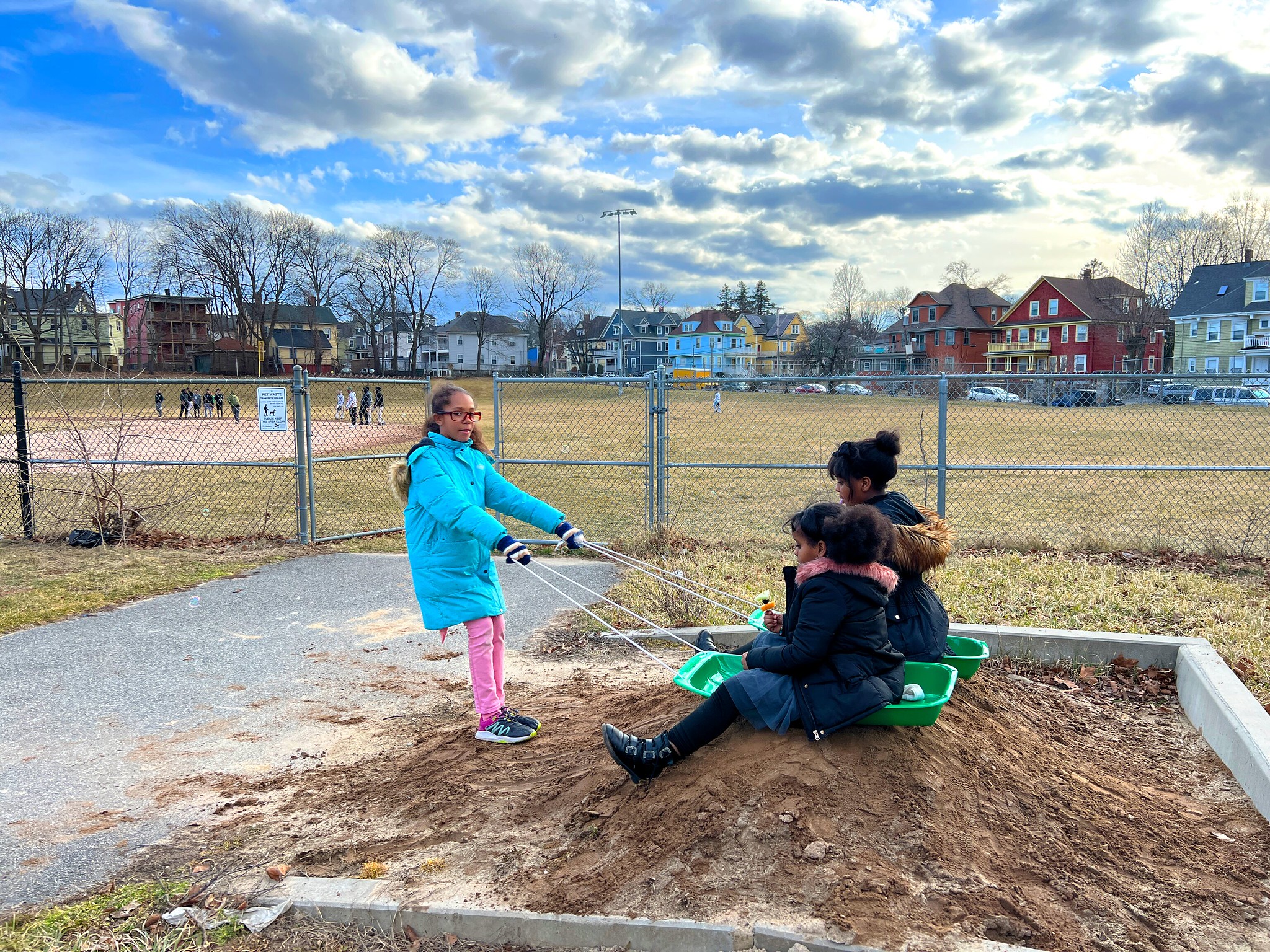 A girl pulls two other young children down a pile of sand on sleds.