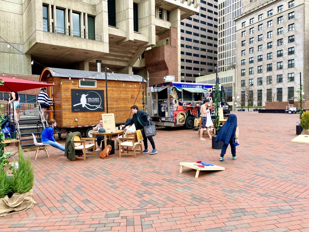 People play corn hole and eat at tables in front of the Winter City Sauna on city hall plaza.