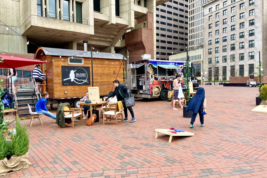 People play corn hole and eat at tables in front of the Winter City Sauna on city hall plaza.
