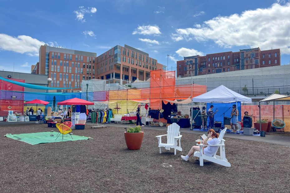 Person reading a book on a white chair surrounded by a market under colorful scaffolding and a band