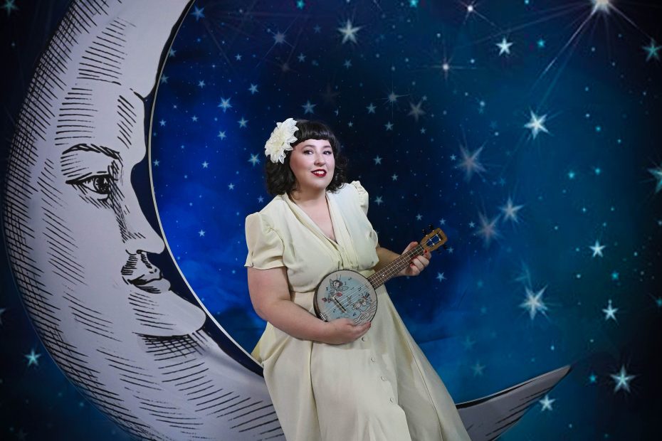 Woman in a white dress sitting on a grey crescent moon against a backdrop of a night sky