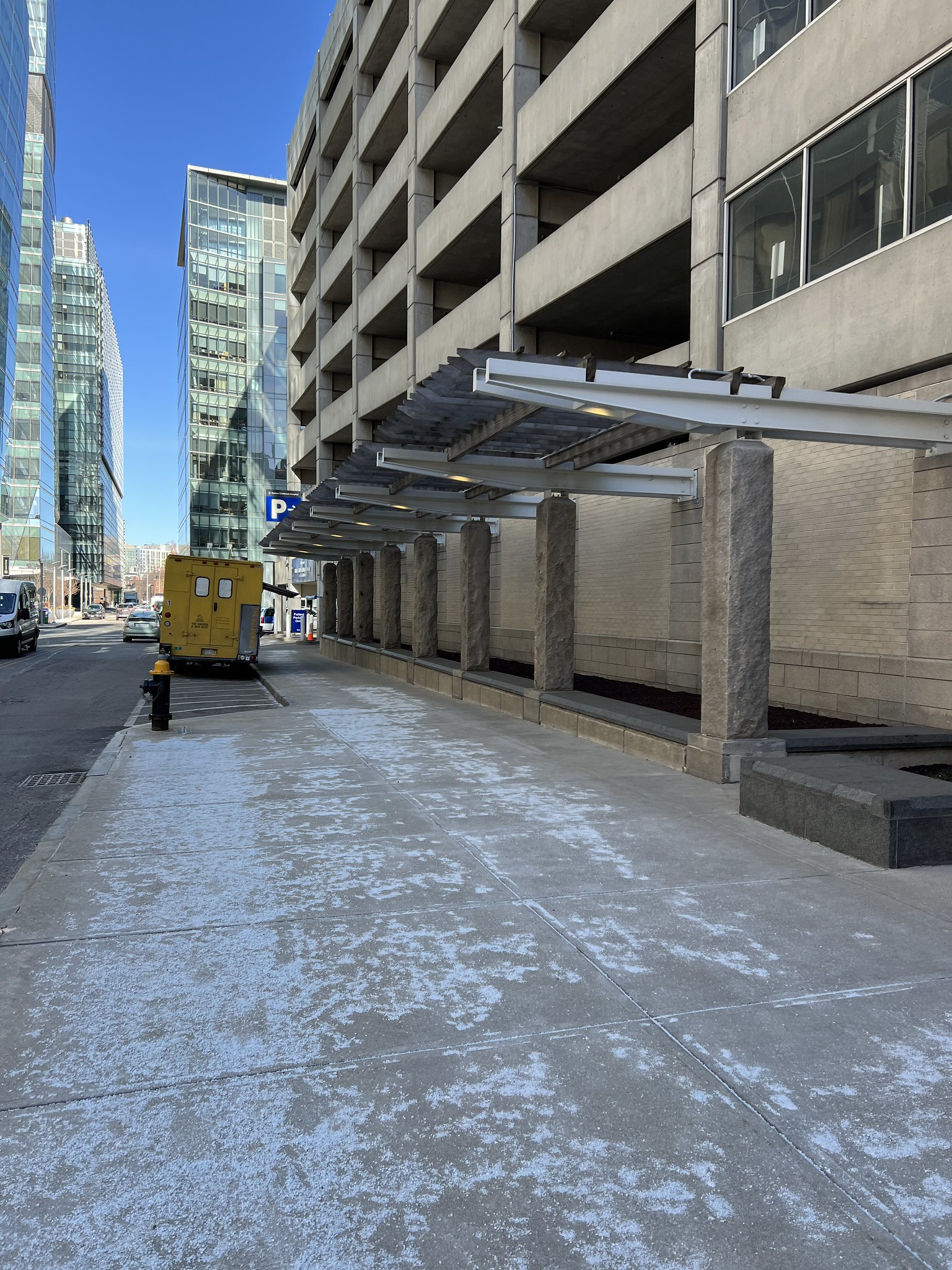 An icey walkway in front of a parking garage with a pergola