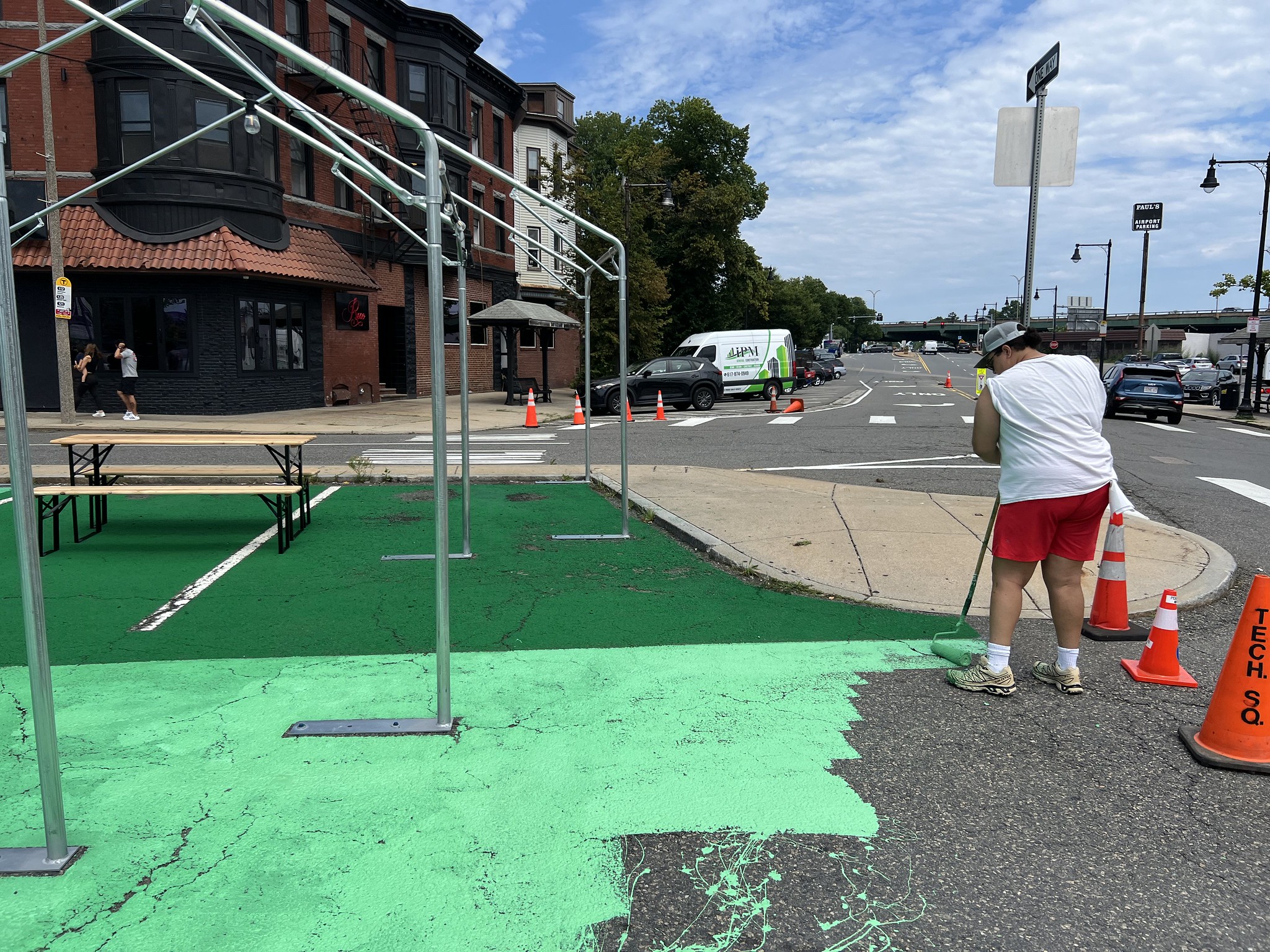 A person stands painting the edge of a parking lot light green 