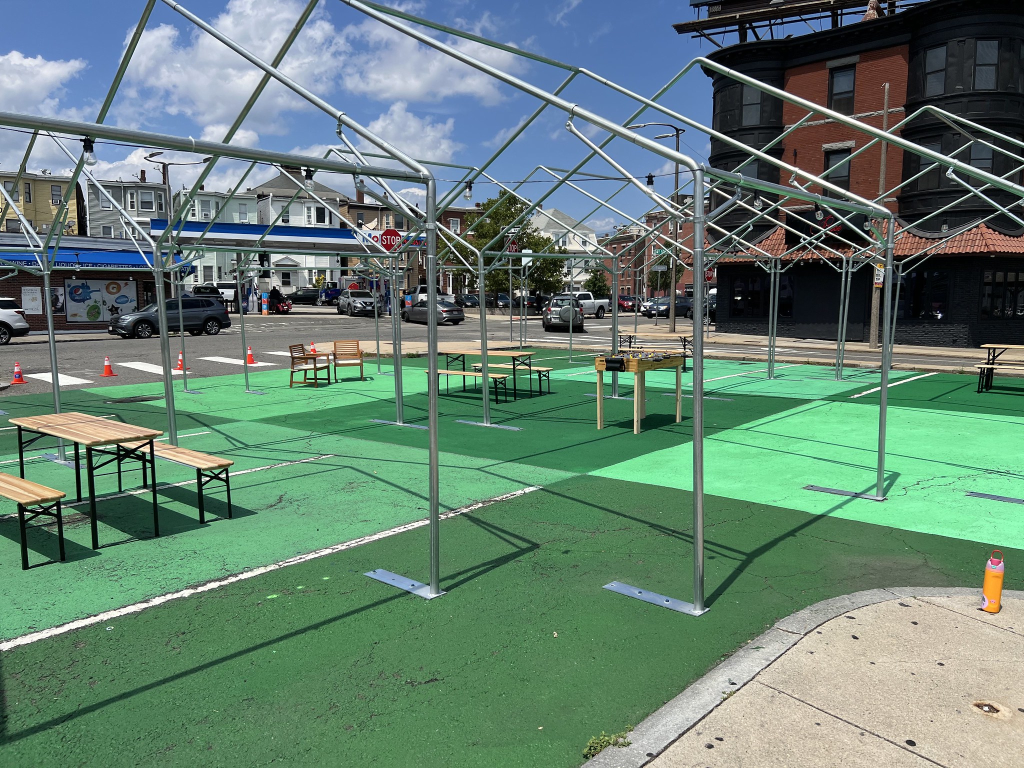 A completed green checkered mural sits with picnic tables, chairs, and a ping pong table. The metal frames of a shade structure are installed above.