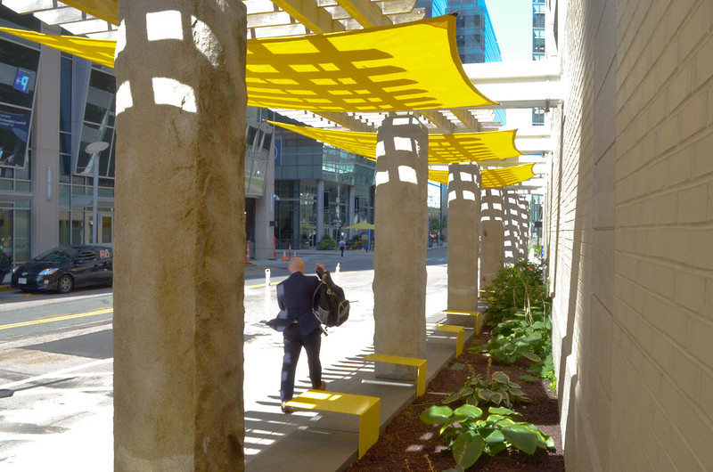 A man walks underneath bright yellow shade sails while picking up his backpack