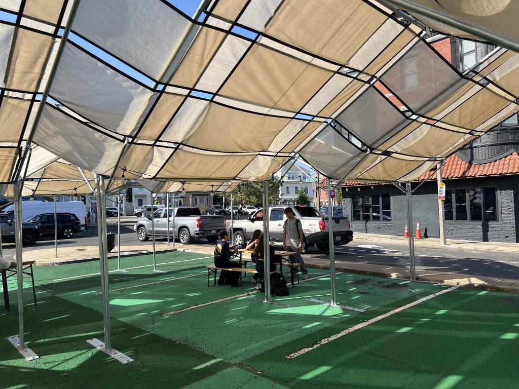 Four teens sit at a picnic table under a tan shade structure on a green ground mural