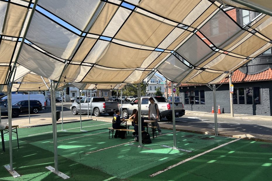 Four teens sit at a picnic table under a tan shade structure on a green ground mural