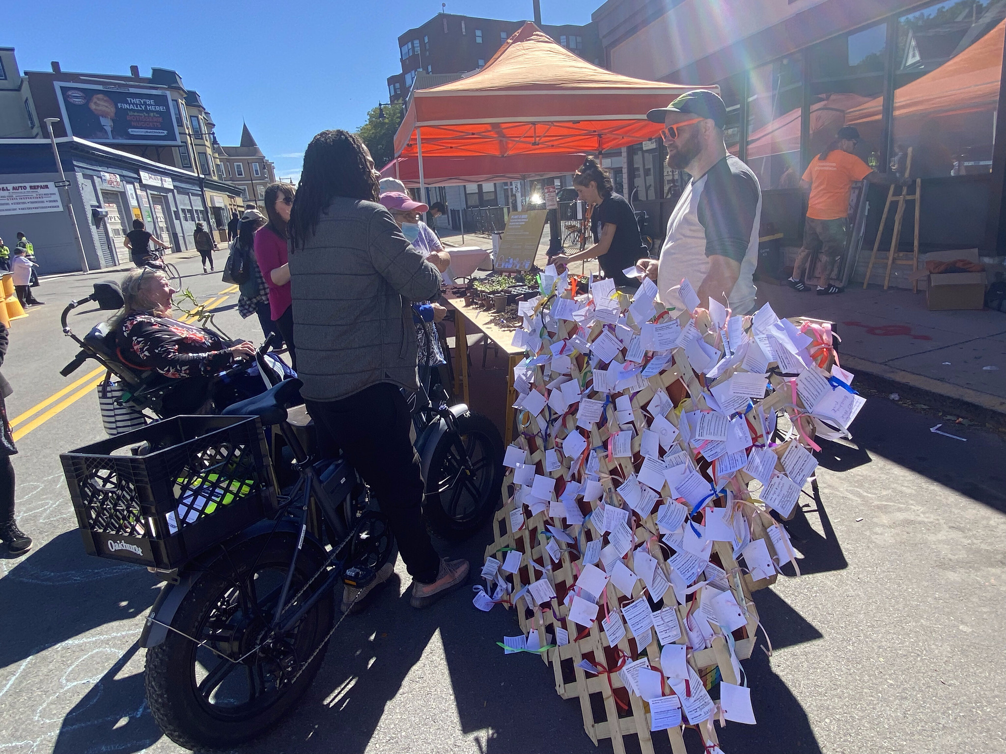 People hand out plants in front of a fence covered in notes