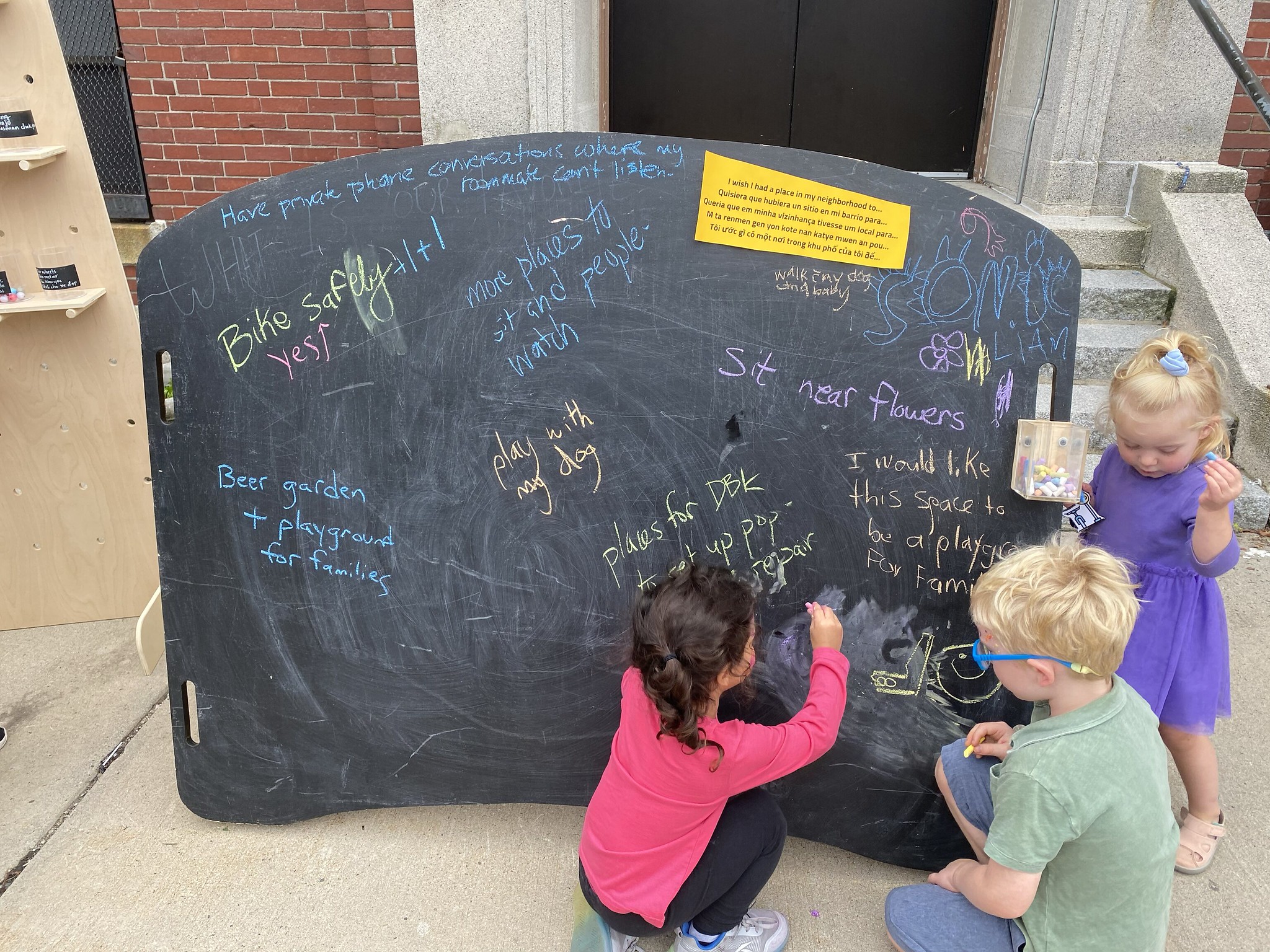 Children kneel in front of a chalkboard that reads "I wish I had a place in my neighborhood to..."