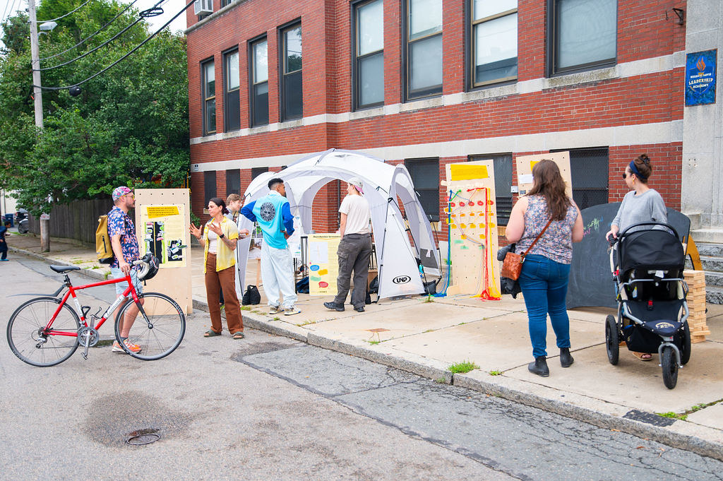 People stand around on the sidewalk and on the street next to data collection tools