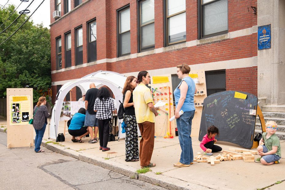 People stand around and chat while children play in front of a chalk board