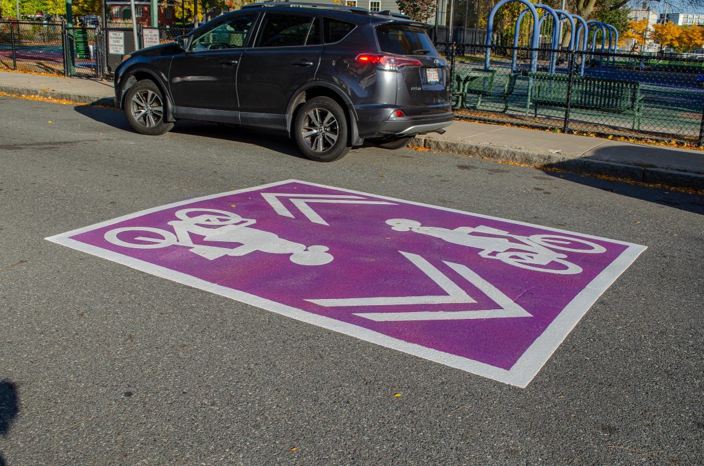 A symbol on a road of a femme-presenting person riding a bike with a purple background.