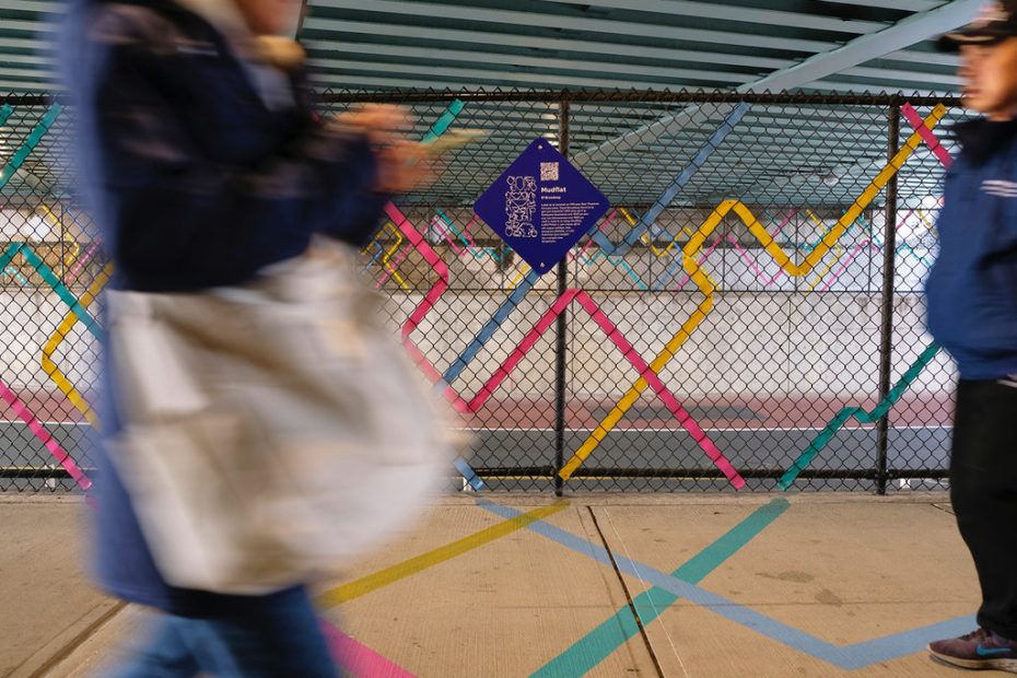 People walk by in front of a colorful fence and on a ground mural