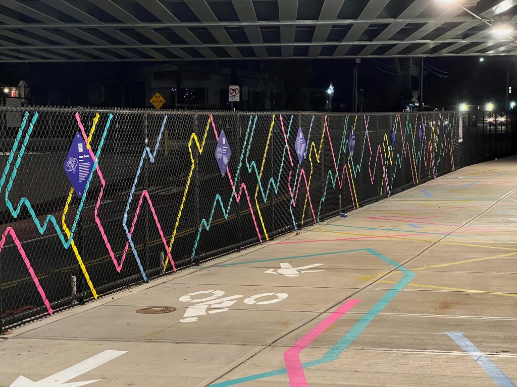 Night time photograph of a walkway with a shared path symbol on the ground alongside a colorful mural