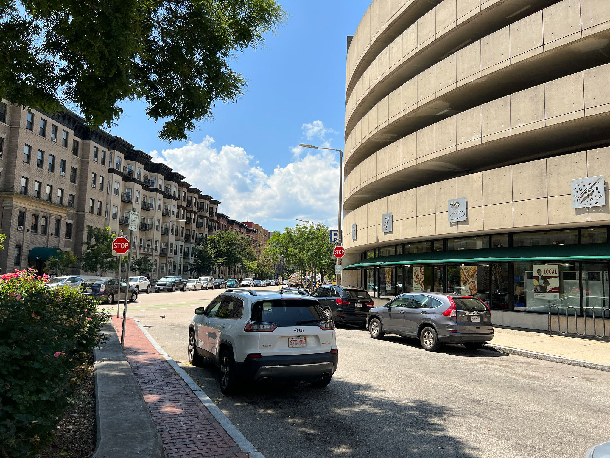 A side view of a street with parked cars on either side and a parking structure in the distance.