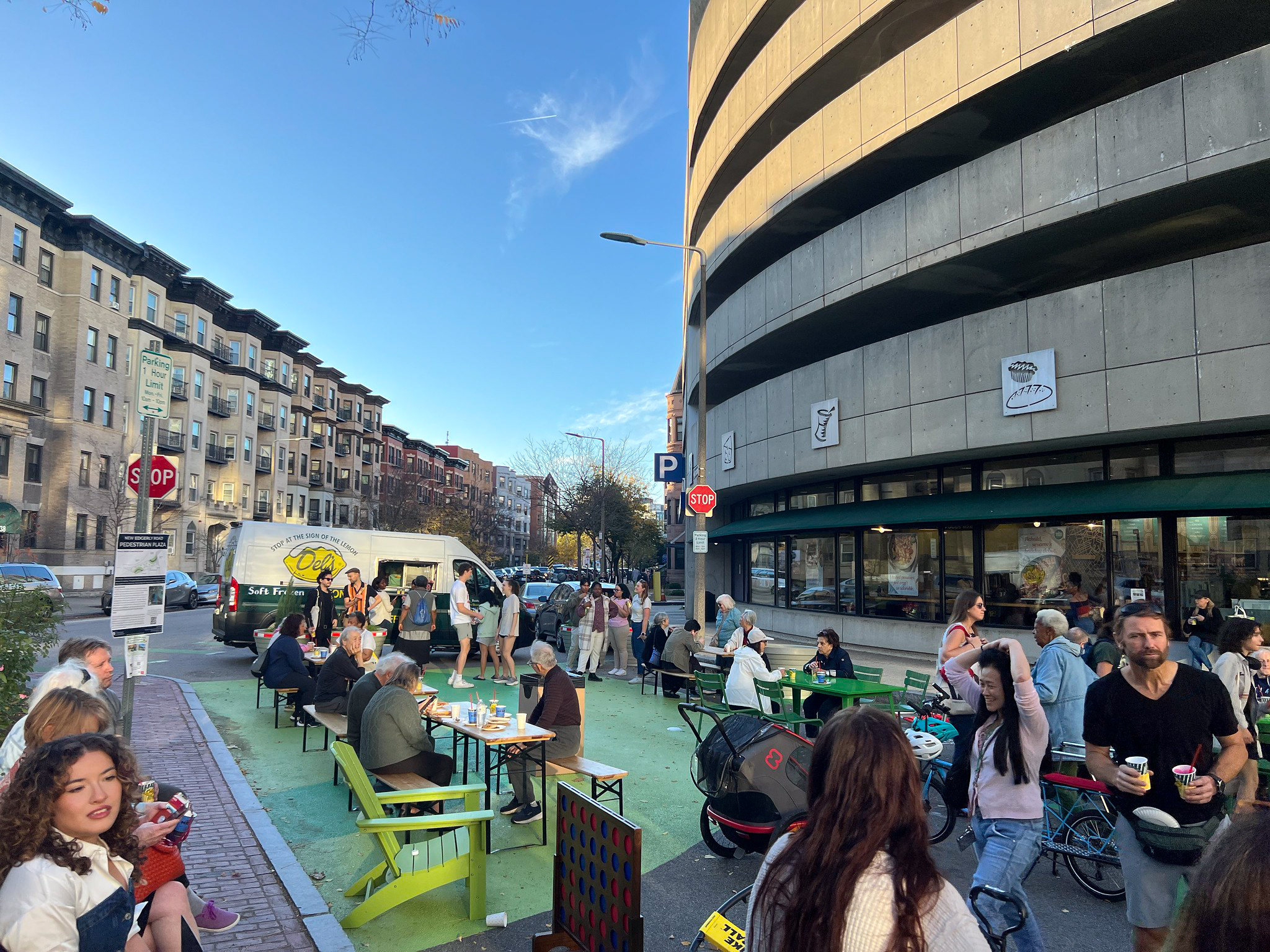 A side view of a street full of people eating and talking on a street mural with a parking structure in the background.