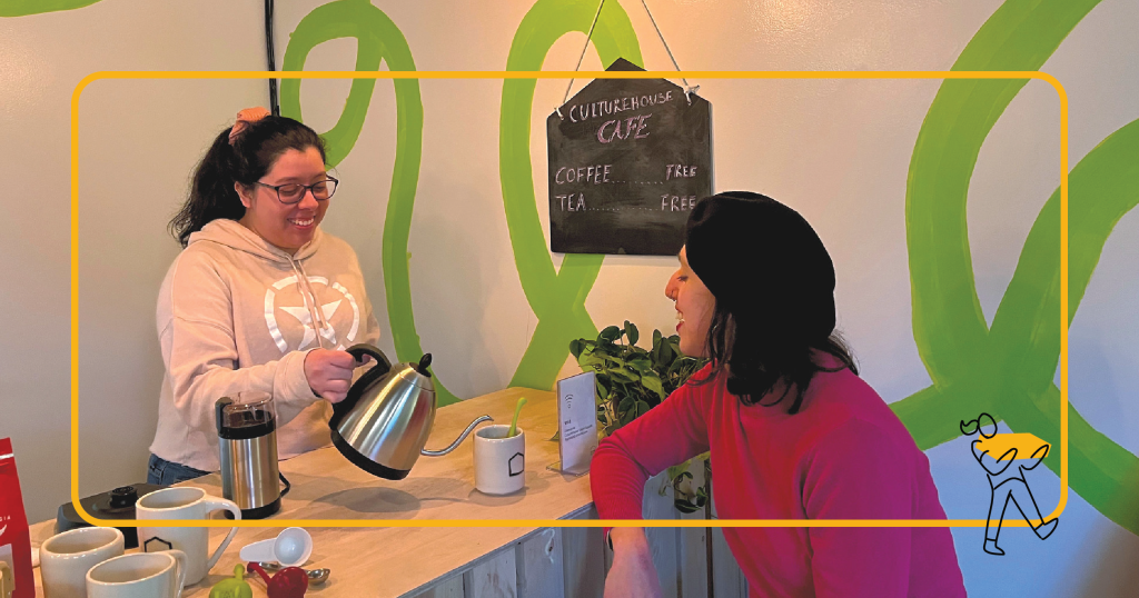 A person making coffee for a woman in a red sweater.