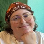 Bianca smiling, wearing a bandana and glasses, with her chin resting on her hand