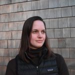 Linnea looking to the upper right of the camera, wearing a black vest, in front of a wood-panel background